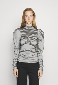 Top lungo manica argento metallizzato con colletto alto, design frontale arricciato e maniche a sbuffo. Abbinato a pantaloni neri, con texture liscia.