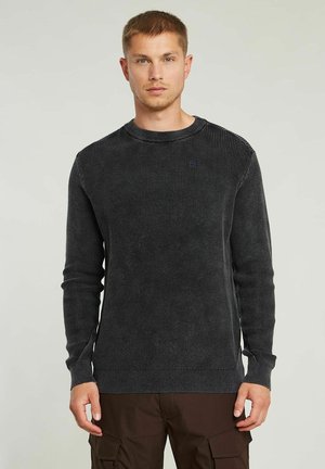 Pull en tricot gris foncé avec une texture côtelée, col rond et manches longues. Petit logo sur la poitrine. Coupe classique.
