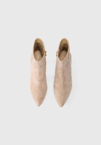 Bottines à bout pointu en daim beige, dotées d'une fermeture éclair sur le côté et d'une texture lisse, avec une silhouette élancée pour un look ajusté.
