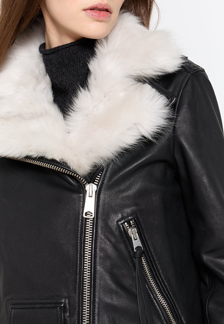 Schwarze Lederjacke mit einem weißen Kunstfellkragen, ausgestattet mit einem silbernen Reißverschluss und mehreren Reißverschlusstaschen. Strukturierte, taillierte Passform.