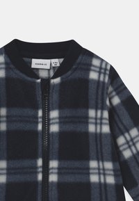 Marineblaues und graues Karomuster-Fleecejacke mit durchgehendem Reißverschluss und geripptem Kragen. Hat eine weiche Textur und ein kontrastierendes weißes Karomuster.