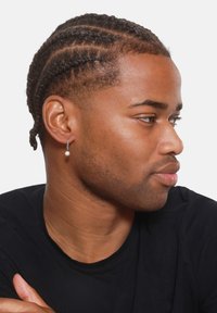 Orecchino a cerchio argento con una piccola perla bianca, indossato da un modello con capelli intrecciati, su uno sfondo bianco semplice, che indossa una maglietta nera.
