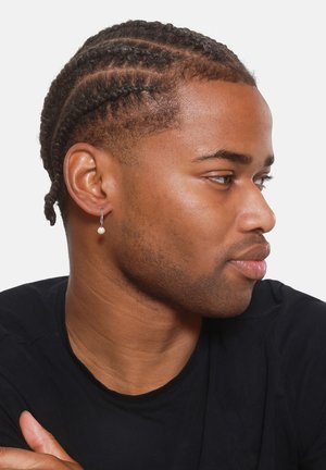 Silberne Creolen mit einer kleinen weißen Perle, getragen von einem Model mit geflochtenem Haar, vor einem schlichten weißen Hintergrund, in einem schwarzen Shirt.