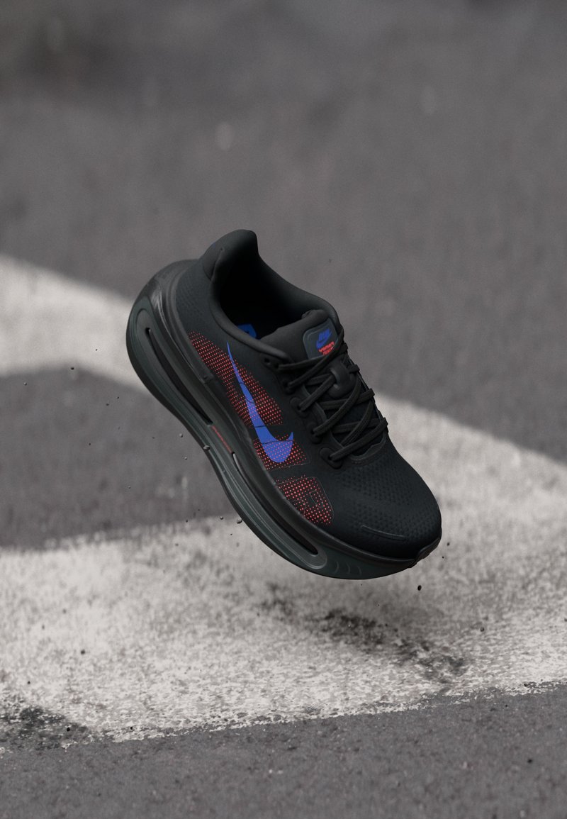 Pantofii sport negri cu un superior din plasă, accente roșii și albastre, talpă texturată și un logo Nike proeminent. Design ușor pentru performanță.