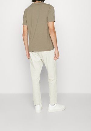 Khaki lyhythihainen paita, pehmeä kangas, miehistön pääntie, yhdistetty vaalean kermanvärisiin housuihin ja valkoisiin lenkkareihin, näkyy rento taka-näkymä.