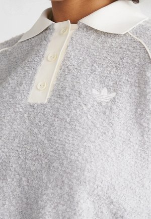 Polo en polaire texturée gris clair avec col blanc, trois boutons et petit logo blanc Adidas sur la poitrine.