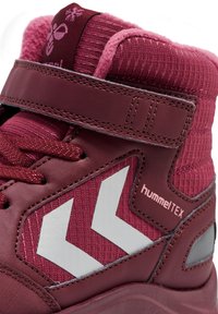 Zapatilla alta en rosa y burdeos con parte superior de punto texturizado, detalles de cuero, correa de Velcro y logo reflectante en forma de chevron.