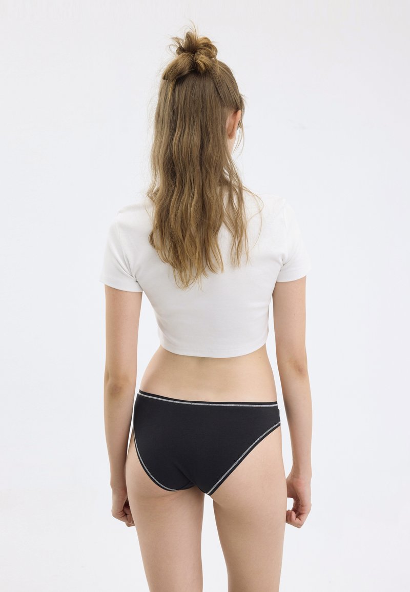 Ropa interior de algodón negra con un ribete elástico blanco en contraste, emparejada con una camiseta corta blanca de manga corta, visible desde la espalda.