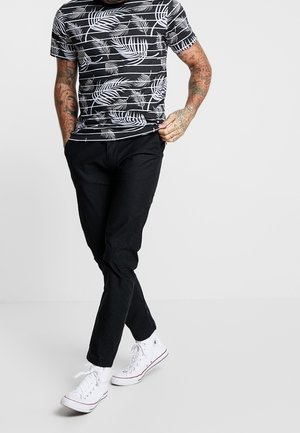 Camiseta de rayas negras y blancas con un patrón de hojas de palma, combinada con pantalones negros y zapatillas blancas. Tejido suave con un ajuste informal.