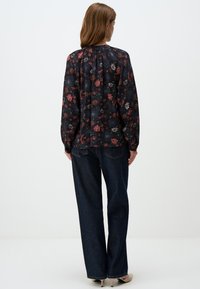 Blusa nera a fiori con maniche lunghe, caratterizzata da una scollatura arricciata e motivi floreali multicolori, abbinata a pantaloni larghi in denim scuro.