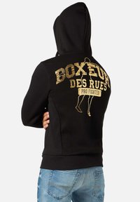 Felpa nera con stampa dorata sul retro che presenta il testo "BOXEUR DES RUES PRO FIGHTER" e una silhouette. Tessuto morbido, vestibilità rilassata.