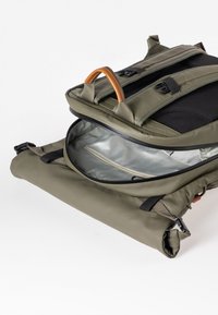 Sac à dos vert olive avec poignée marron, compartiment principal ouvert révélant un intérieur argenté avec une poche zippée.