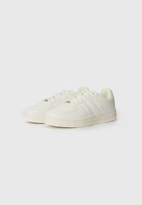 White leather sneakers with textured surface, round toe, flat sole, and three accent stripes on the sides. Laces and perforated detailing present.