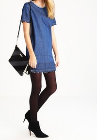 Robe en denim à manches courtes, bords effilochés et coupe droite. Associée à un sac à main rayé noir et blanc et à des collants noirs.
