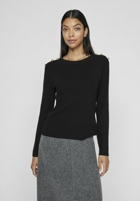 Pull noir à manches longues côtelé avec des boutons dorés aux épaules, associé à une jupe grise texturée. Design simple et ajusté.
