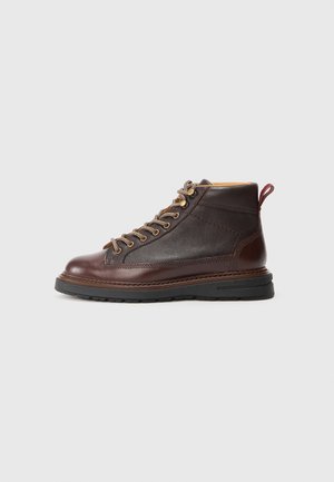 Bruine leren enkelboots met een gestructureerde bovenkant, contrasterende gladde neus, metalen veters en een robuuste rubberen zool. Een trekband aan de achterkant is inbegrepen.