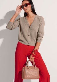 Beige geribbelde cardigan met knopen, rode high-waisted broek, rode armband en een geweven rosé handtas met dubbele handvatten.
