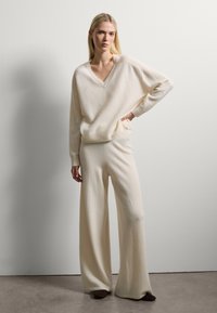 Suéter de punto color crema con escote en V y puños acanalados, combinado con pantalones de pierna ancha, ambos suaves y texturizados.