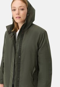 Olivenfarvet parka-jakke med lynlås og trykknaplukning, hætte og sidelommer. Glat tekstur og funktionelt design med minimal dekoration.