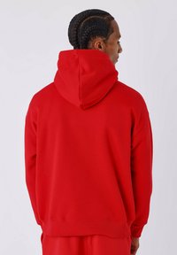 Sudadera roja con un corte holgado, capucha ajustable con cordón y puños acanalados. Textura suave con un color sólido y sin patrones visibles.