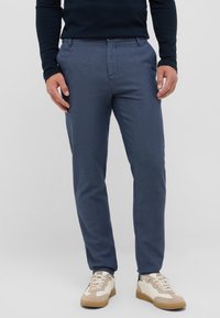 Granatowe spodnie o fakturowanym wykończeniu, slim fit, z bocznymi kieszeniami, noszone z beżowymi i białymi sneakersami.