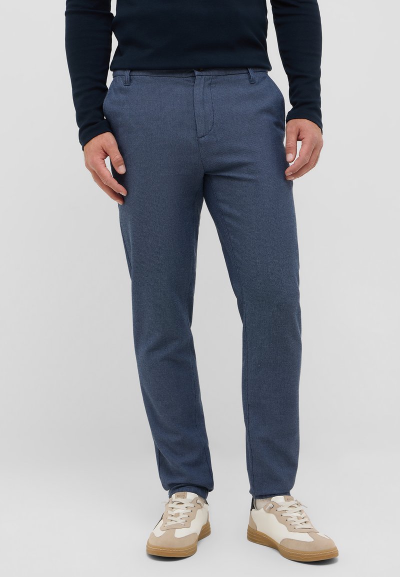 Granatowe spodnie o fakturowanym wykończeniu, slim fit, z bocznymi kieszeniami, noszone z beżowymi i białymi sneakersami.