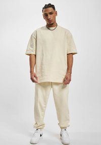 Cream-colored oversized t-shirt with short sleeves and matching joggers, made from soft fabric. Paired with white sneakers featuring black accents.