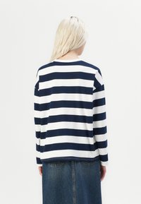 Navy and white striped long-sleeve top with a round neck, featuring a relaxed fit and dropped shoulders, paired with a denim skirt.