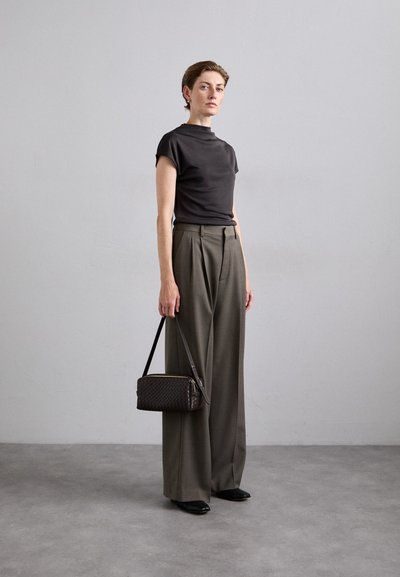 Dark gray short-sleeve top, olive green high-waisted trousers, black pointed shoes, and a woven dark bag with a shoulder strap.