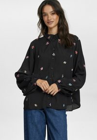 Schwarze Bluse mit floraler Stickerei in Pink, Lila und Blau. Verfügt über eine durchgängige Knopfleiste, weite Ärmel und ein klassisches Kragendesign.