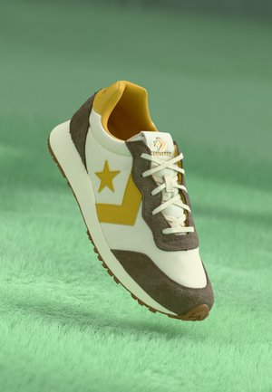 Sneaker featuring a white leather upper, brown suede accents, yellow star and logo, with a textured brown rubber sole and white laces.