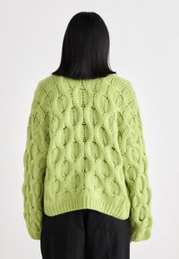 Πλεκτό πουλόβερ σε φωτεινό λάιμ πράσινο με σχέδιο καμπάνας, χοντρή υφή και ριμπ τελείωμα. Μακριά, φαρδιά μανίκια με χαμηλούς ώμους.