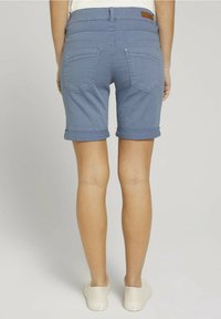 Shorts in denim blu con risvolti, due tasche posteriori e un dettaglio in pelle in vita, abbinati a sneakers bianche.