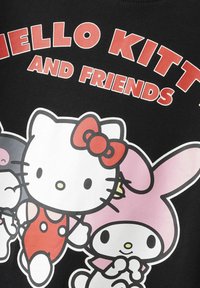 T-shirt grafico nero con Hello Kitty e i suoi amici in colori vivaci. Accenti rossi notevoli con un design giocoso e testo audace.
