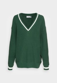 Pull vert en maille avec col en V, orné de rayures blanches sur le col et les poignets. Coupe oversize, tissu texturé.