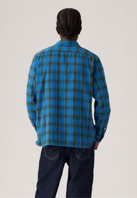 Blauw geruit overhemd met een button-down kraag, voorzien van groene en gele accenten. Lange mouwen en een relaxte pasvorm, gemaakt van zachte stof.