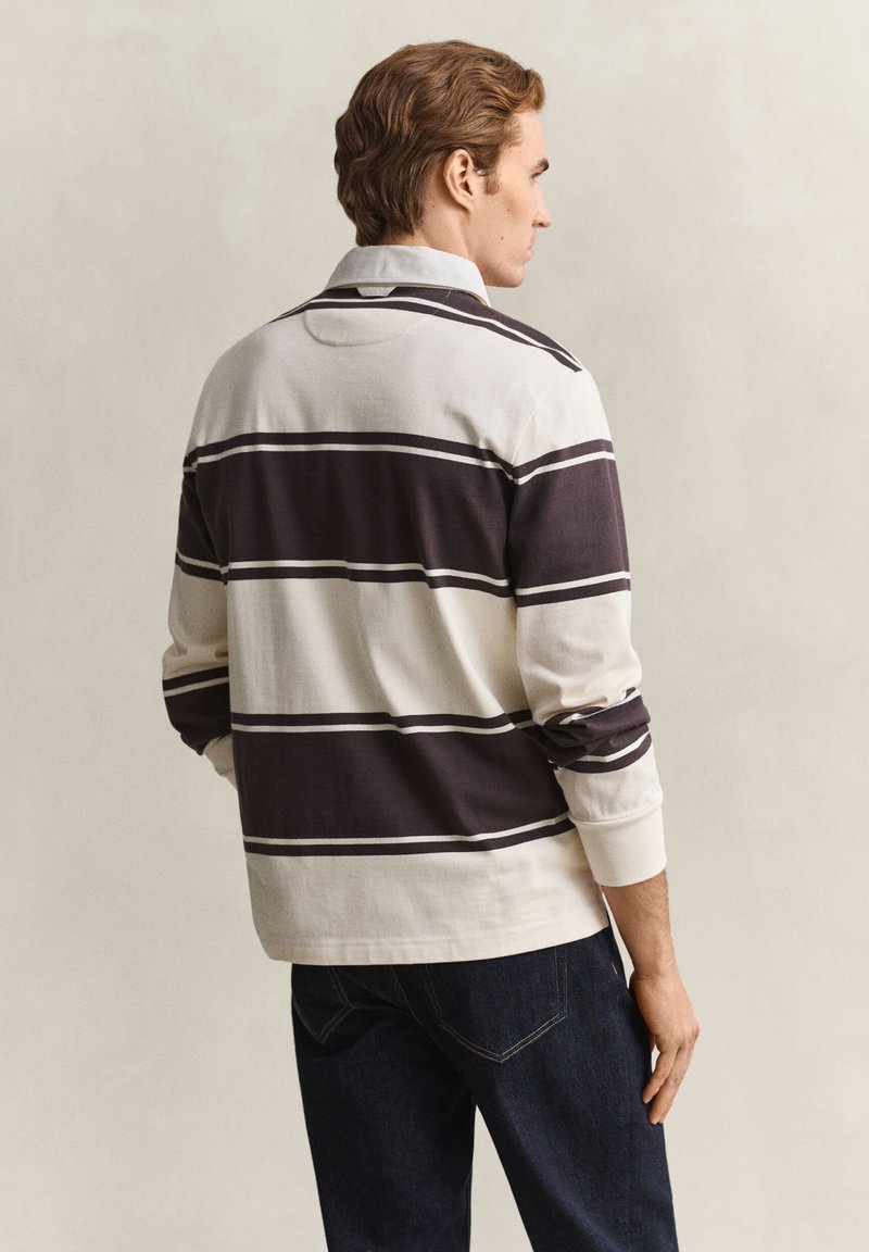 Man facing sideways wearing a long-sleeve rugby shirt with wide black and white horizontal stripes and dark blue jeans.