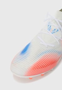 Bota de fútbol blanca con patrones en degradado azul y naranja, cordones blancos y superficie superior texturizada para un mejor control del balón.