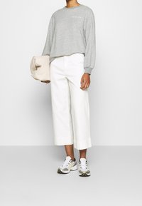 Harmaa pitkähihainen collegepaita yhdistettynä valkoisiin lyhennettyihin leveälahkeisiin housuihin. Kädessä vaalea tikattu laukku ja jalassa valkoiset lenkkarit keltaisin yksityiskohdin.