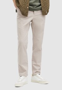Vaaleanbeige puuvillahousut, slim fit -malliset, sileät ja vähäisellä ompeleella. Yhdistetty valkoisiin lenkkareihin siistin ilmeen saavuttamiseksi.