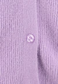 Lila texturierter Strickstoff mit einem einzigen glänzenden Knopf mit vier Löchern, der in der Mitte angenäht ist.