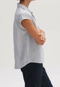 Vaaleansininen lyhythihainen paita, jossa on hienovaraisia pystyraitoja, kaulus ja rento istuvuus. Kangas näyttää pehmeältä hieman teksturoidulla pinnalla.