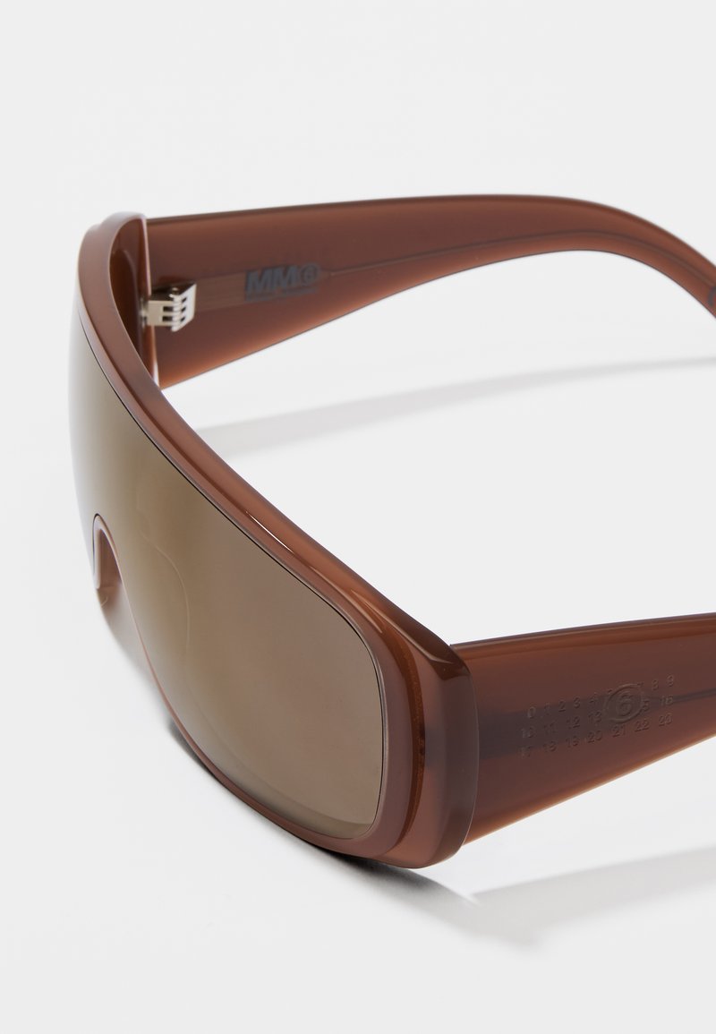 Braune Kunststoffsunglasses mit großen getönten Gläsern und elegantem Wraparound-Design. Merkmale sind ein strukturierter Bügel und ein metallischer Scharnier.