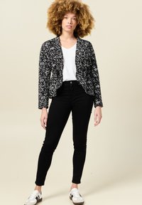 Blazer de patrón floral en blanco y negro con un corte entallado, combinado con una camiseta blanca, pantalones negros y zapatillas blancas.