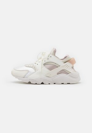 Baskets de sport basses blanches avec panneaux en mesh et cuir, lacets et semelle robuste, vues de côté sur un fond uni.