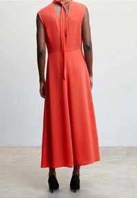 Rotes, ärmelloses Maxikleid mit tailliertem Oberteil, offener Rückseite und Bindeband am Hals. Glattes Material und fließender Rock mit vollem Saum.