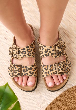 Sandales en imprimé léopard avec deux boucles ajustables, en suède beige, conçues pour les pieds ouverts, et semelle en caoutchouc plate. Fini avec une texture naturelle.