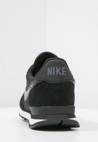 Zapatilla negra de Nike vista desde atrás, con parte superior de malla y ante, entresuela blanca y suela exterior negra.