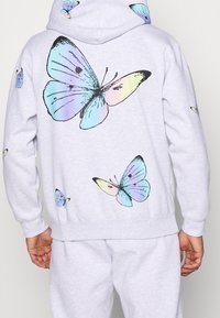 Grauer Hoodie mit großen, mehrfarbigen Schmetterlingsmotiven auf dem Rücken und kleineren auf den Ärmeln; aus weichem Stoff gefertigt.