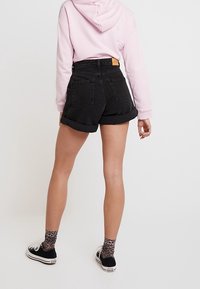 Mustat farkkushortsit, joissa on käännetyt lahkeet, korkea vyötärö ja kaksi takataskua. Yhdistetty vaaleanpunaiseen huppariin ja mustiin lenkkareihin, joissa on kuvioidut sukat.